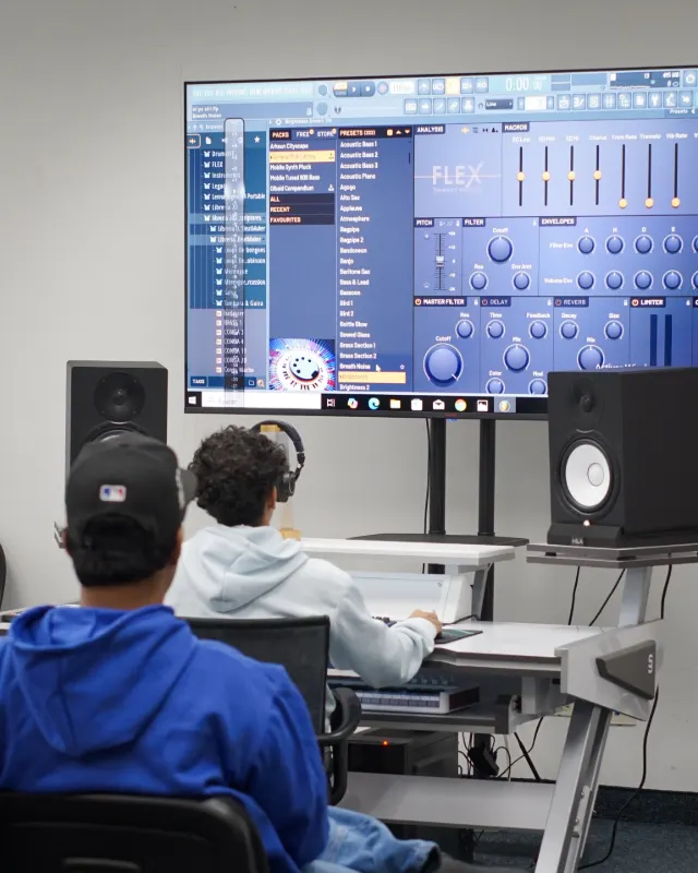 Escritorio de producción con FL Studio en pantalla, monitores de estudio y una persona trabajando